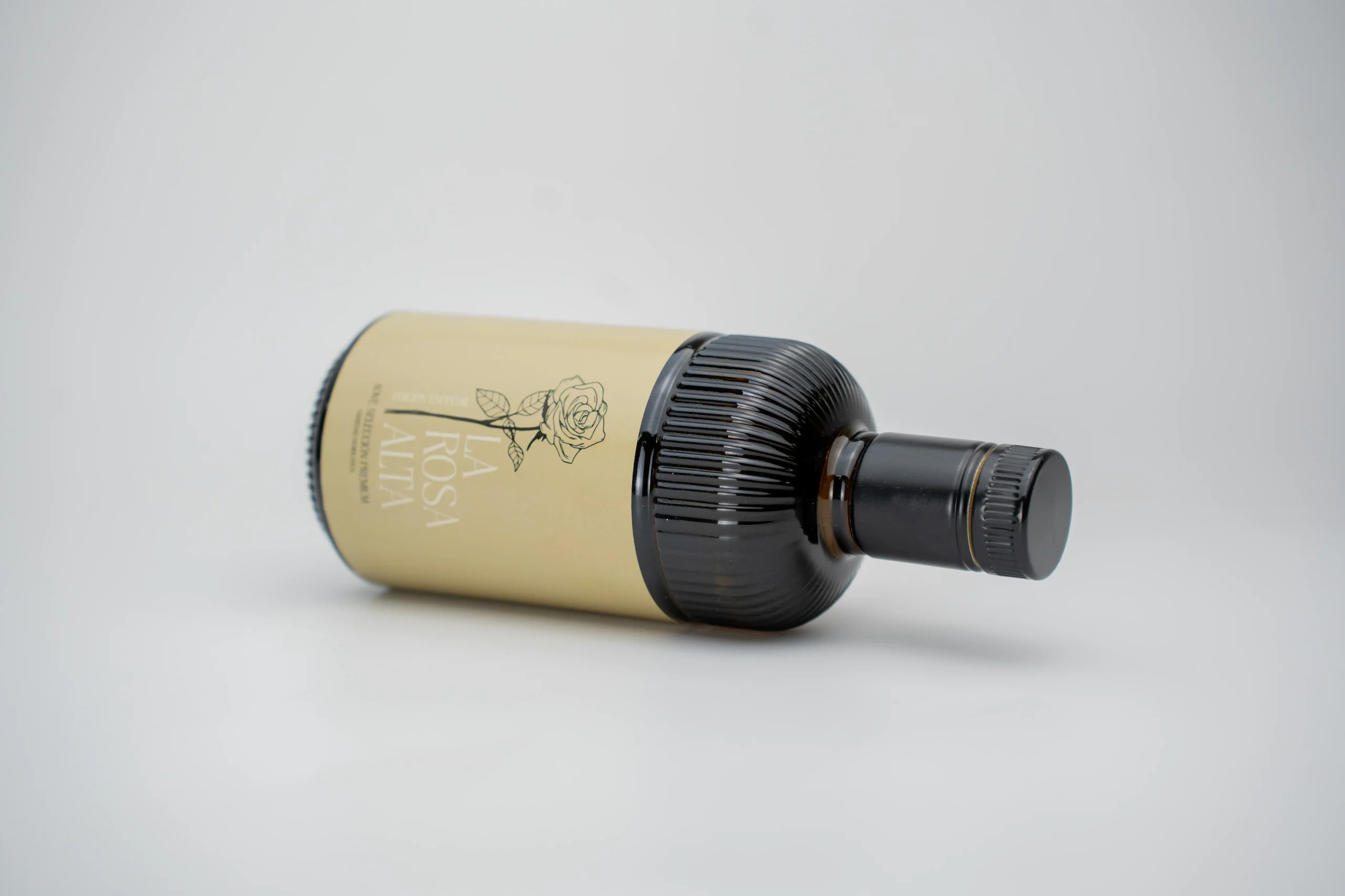 Botella de aceite de oliva virgen extra La Rosa Alta edición especial tumbada sobre fondo grisáceo